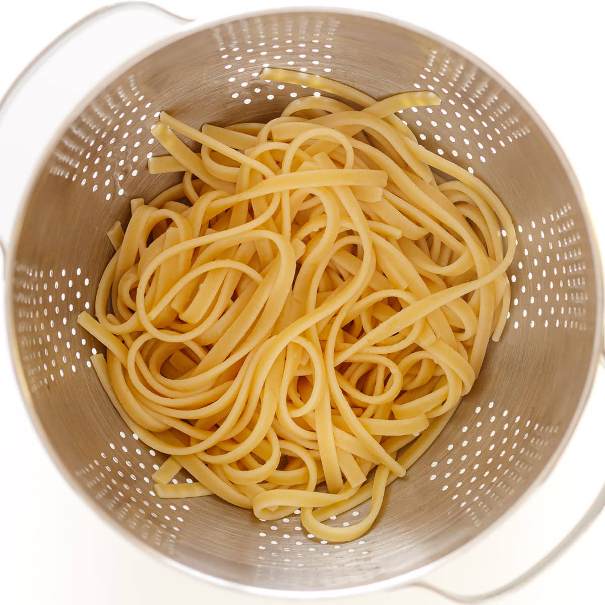 Cooked fettuccine in a stainless steel strainer.
