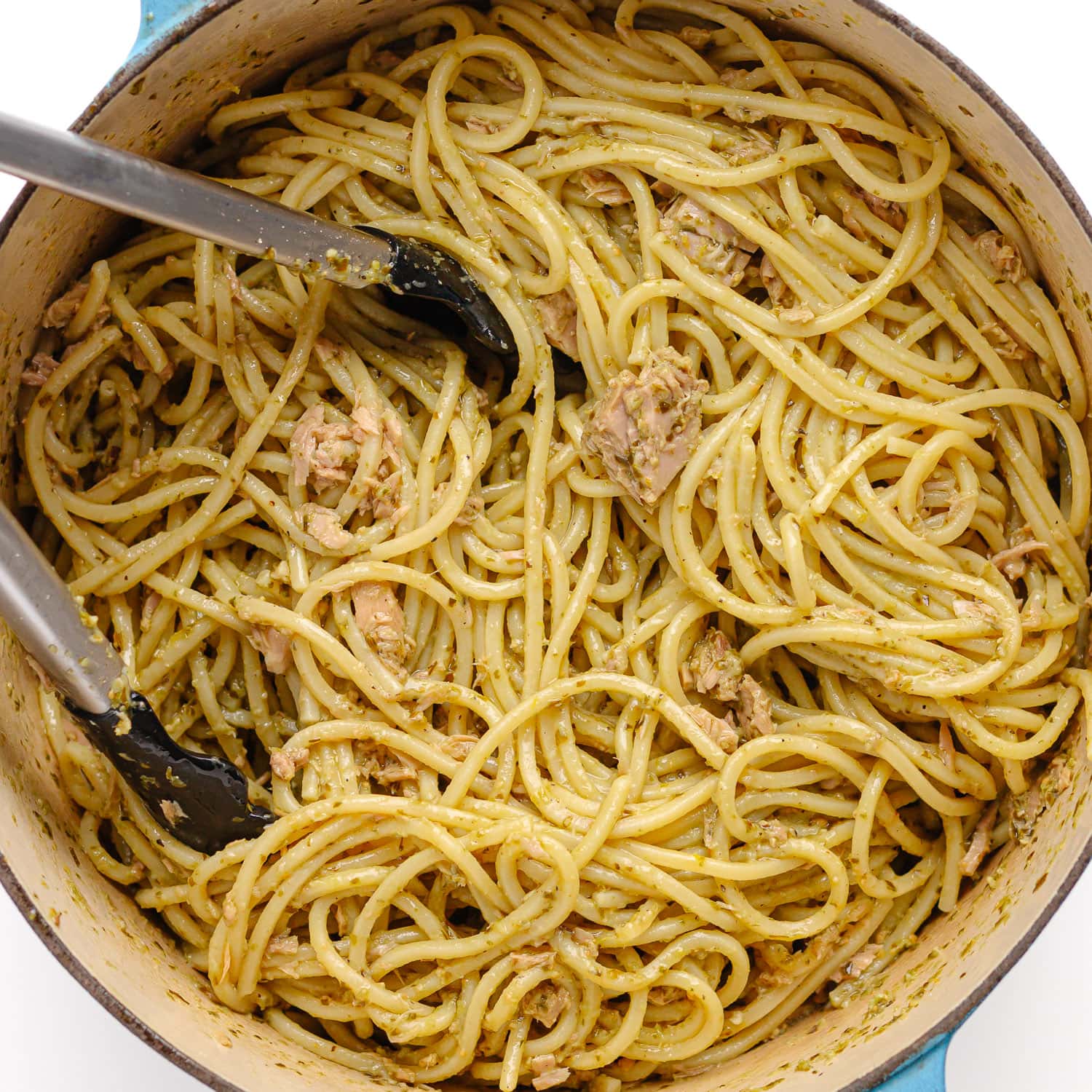 Tongs tossing tuna pesto spaghetti in a dutch oven.