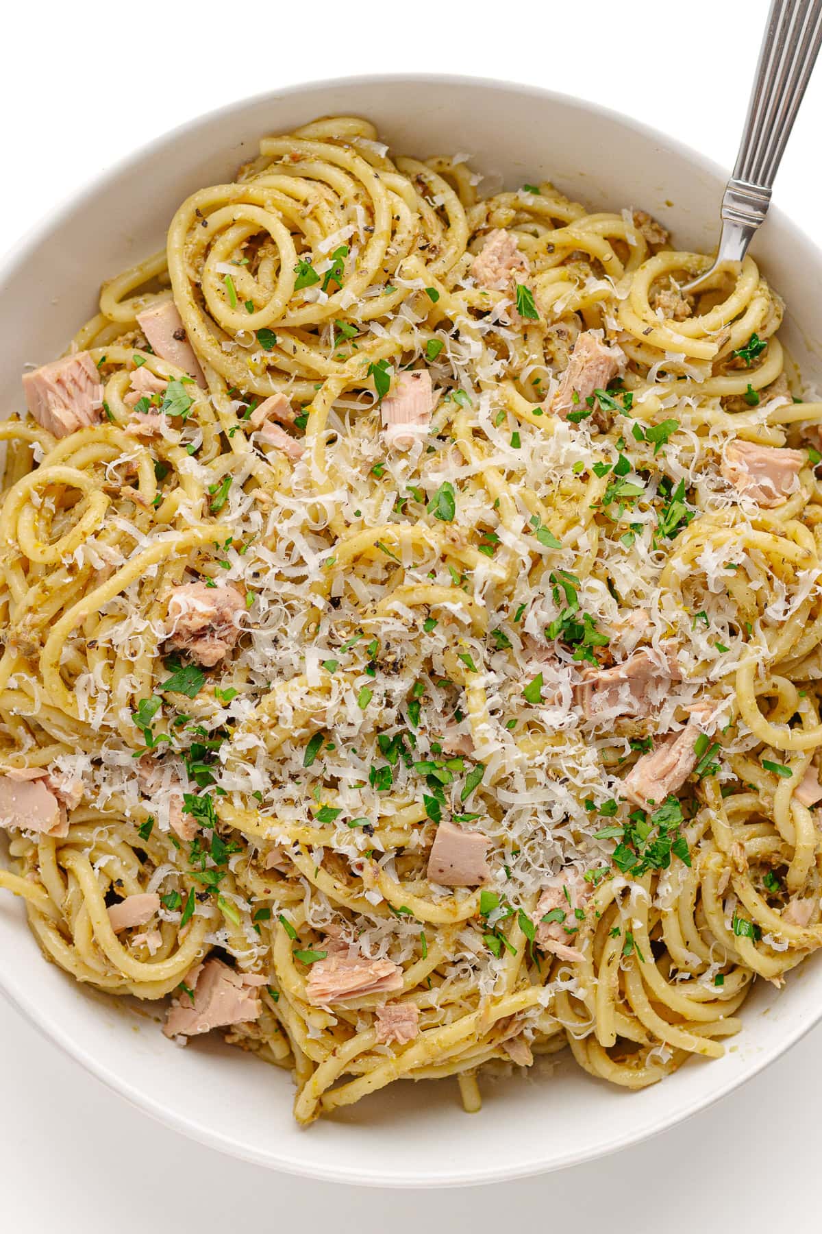 White bowl of tuna pesto spaghetti garnished with parmesan and chopped parsley.