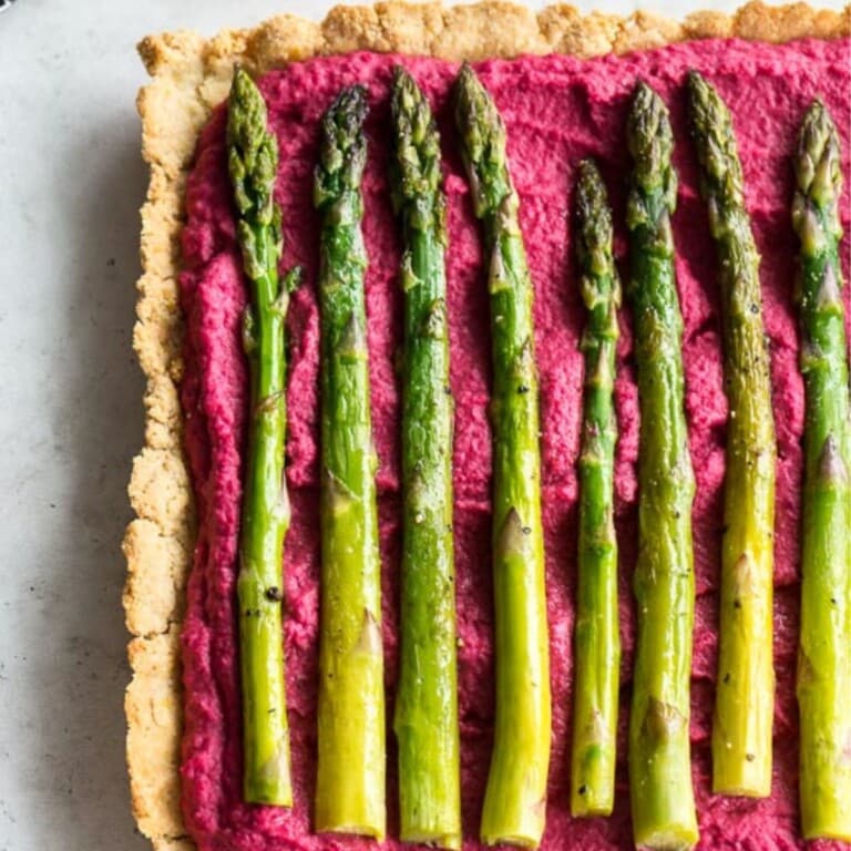 Almond crust tart topped with beet hummus and asparagus stalks.