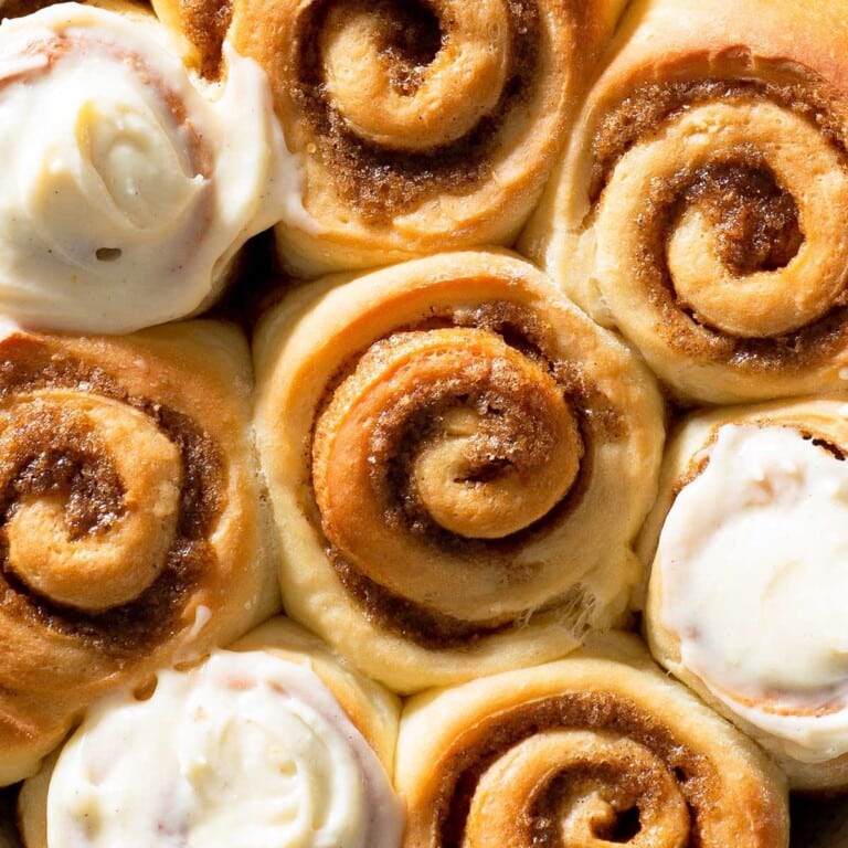 Closeup of cinnamon rolls, some topped with cream cheese frosting.