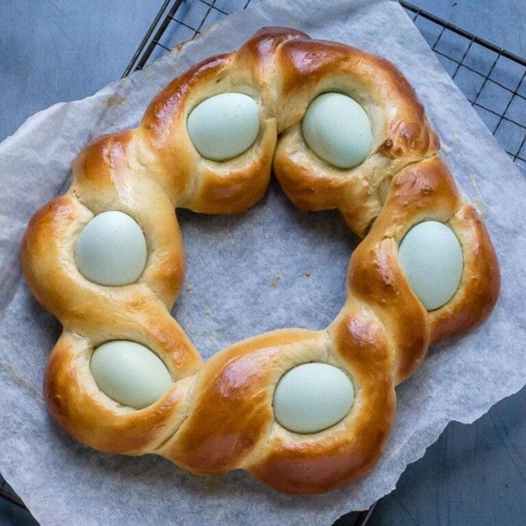 Italian braided Easter bread with pale blue eggs sitting on a parchment paper lined wire cooling rack.