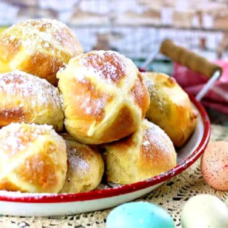 A pile of white chocolate hot cross buns on a serving plate.