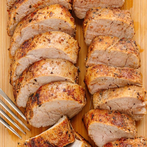 Sliced cast iron pork tenderloin on a wood board with a fork.