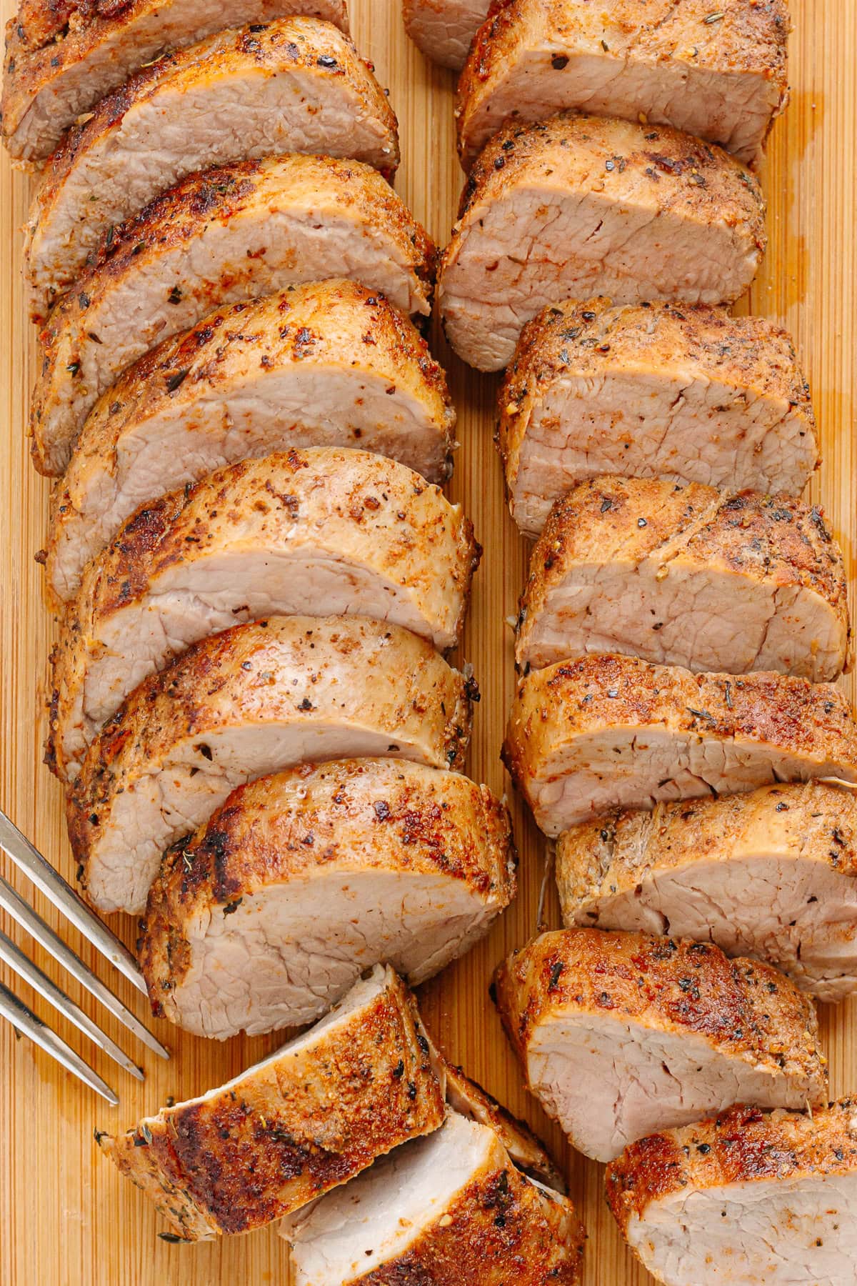 Sliced up cooked pork tenderloin on a wood board with a fork.