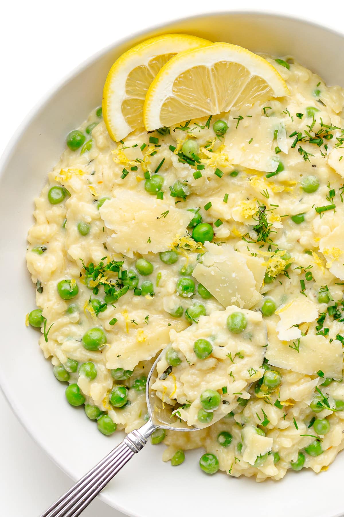 Pea risotto in a white bowl garnished with lemon slices.