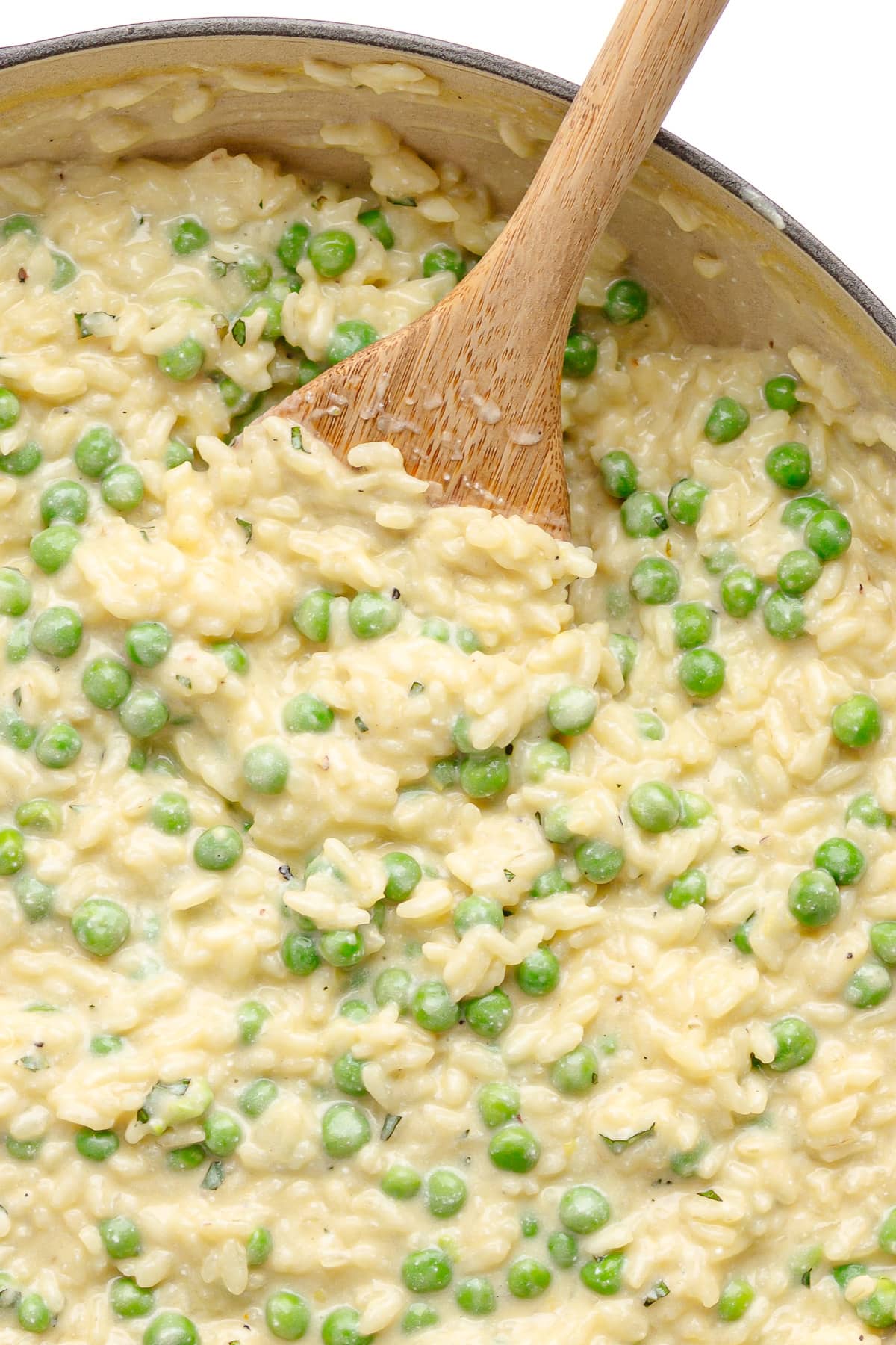 Pea risotto being stirred with a wooden spoon.