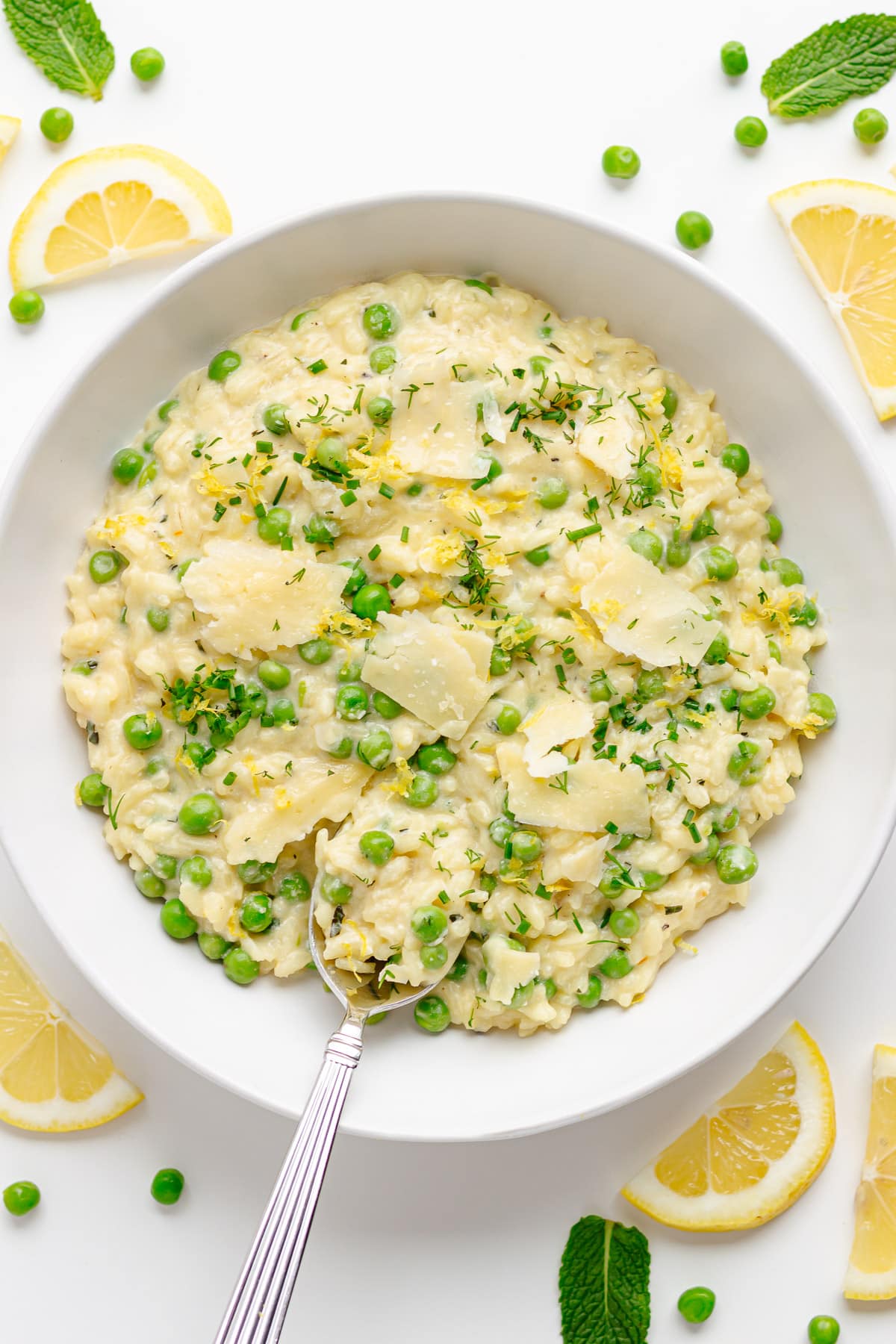 Pea risotto in a white bowl with lemon slices, peas and mint scattered around it.