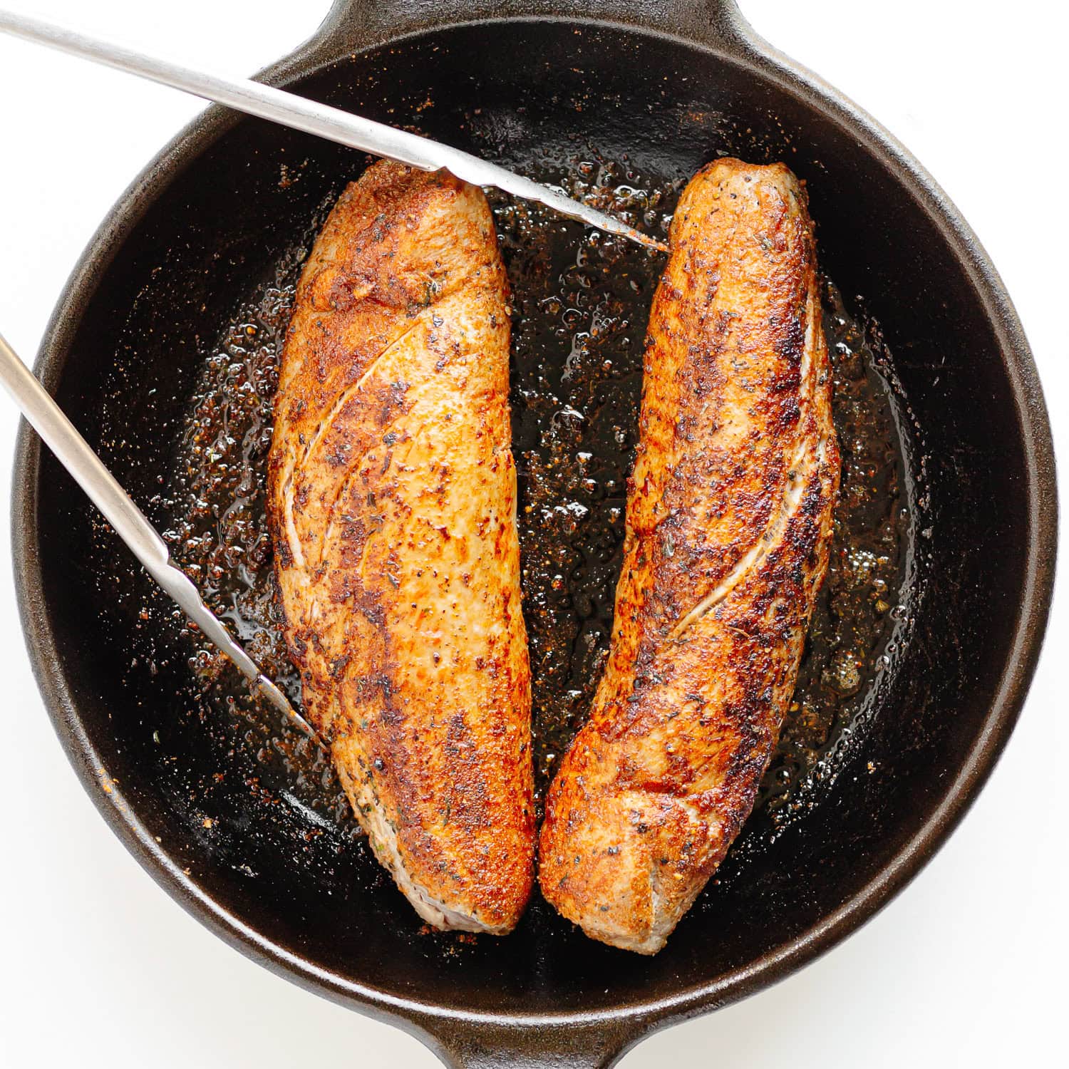 Two pork tenderloin being seared in a cast iron skillet.