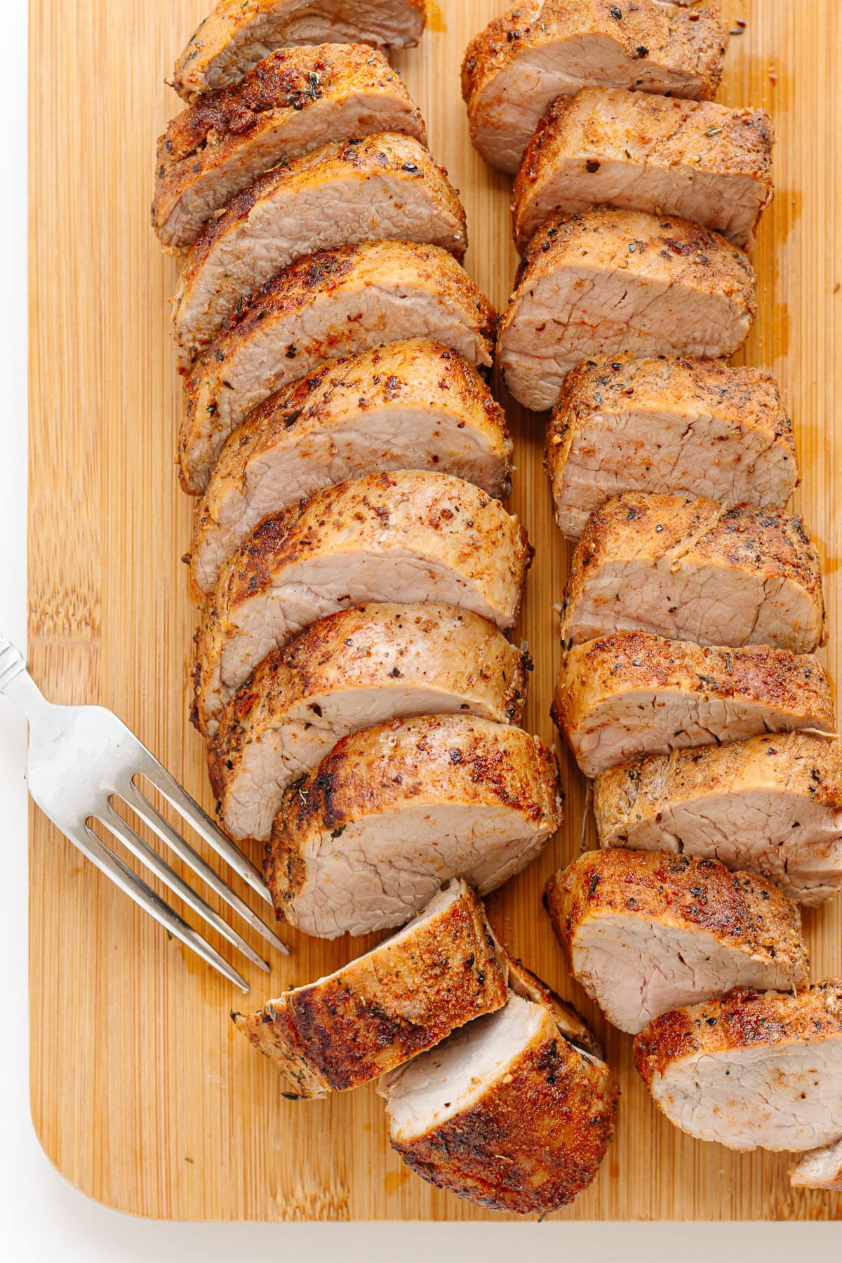 Sliced pork tenderloin on a wood cutting board with a fork.