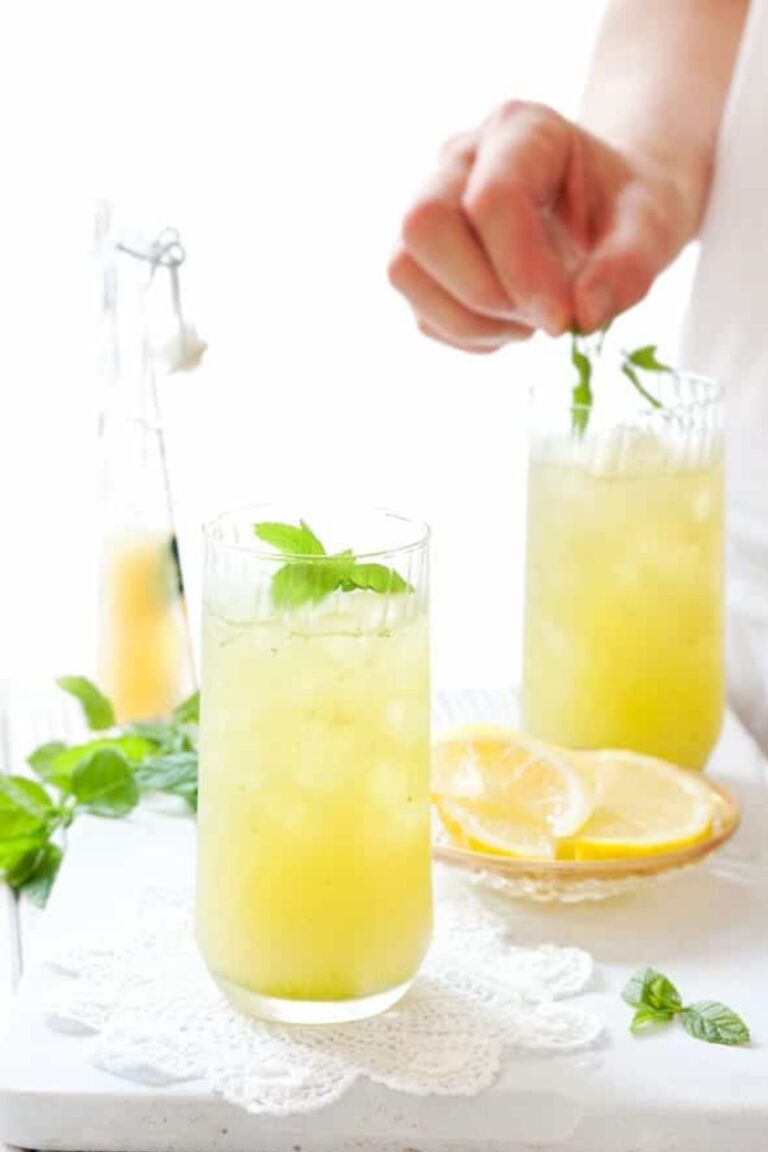 Person adding some garnish to glasses of apple lemon mint cooler.