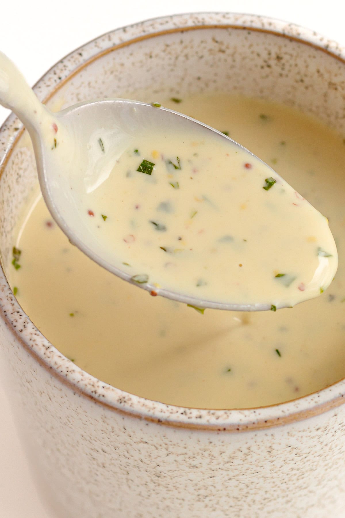 Spoon lifting creamy Dijon sauce out of a sauce jug.