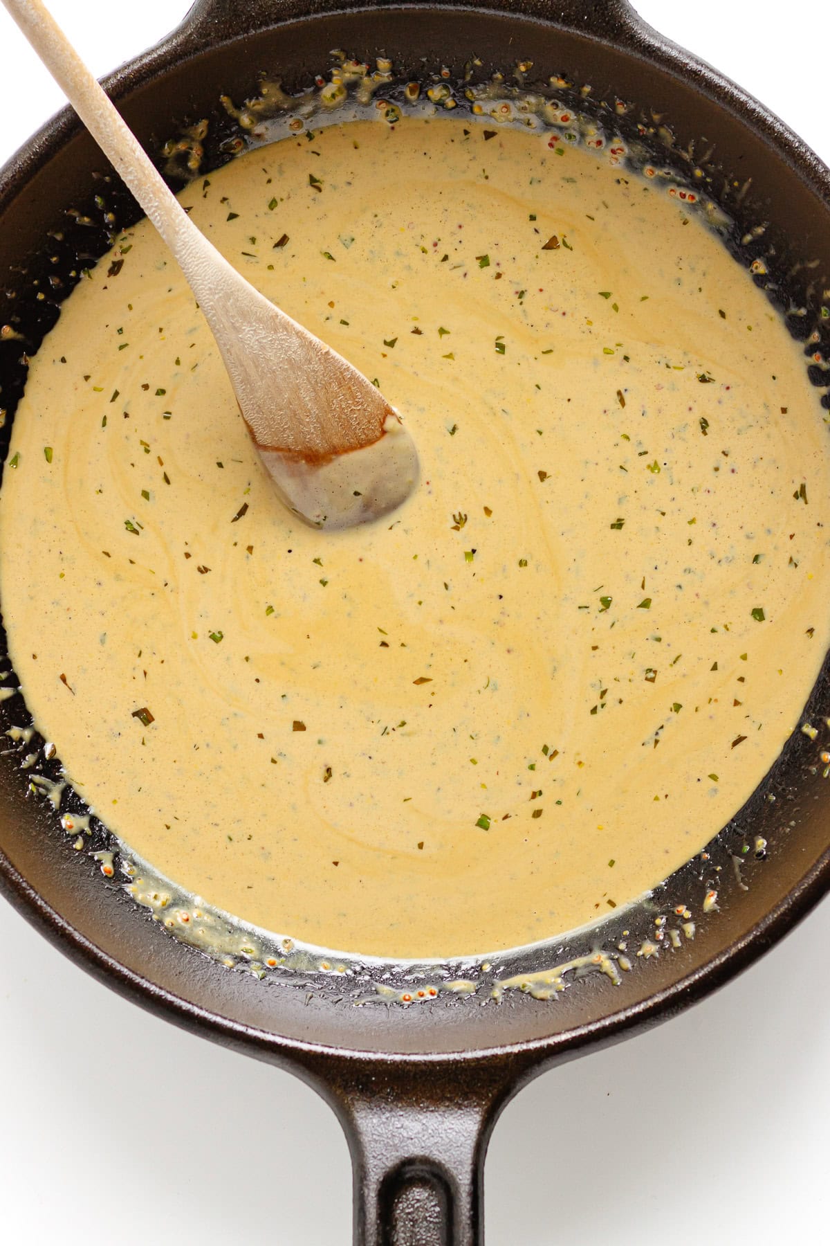 Creamy mustard pan sauce in a cast iron skillet with wooden spoon.