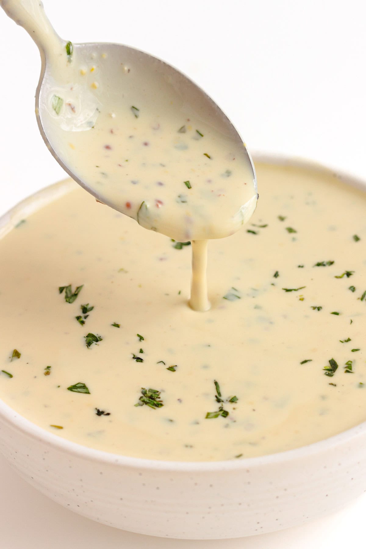 Spoon of Dijon Mustard Sauce drizzling into a small white bowl filled with the same sauce.