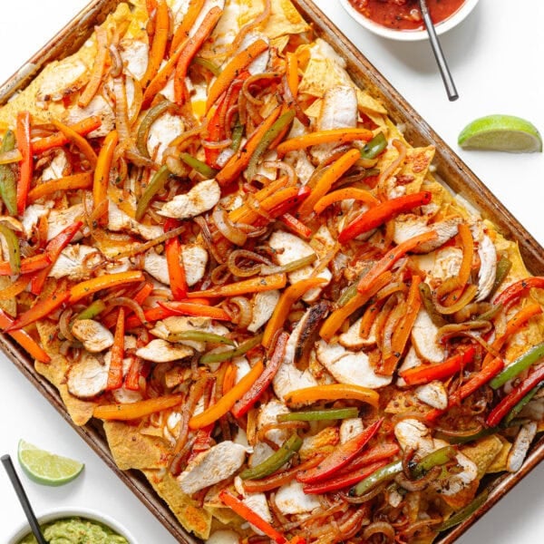 Fajita nachos on a sheet pan with toppings next to it.