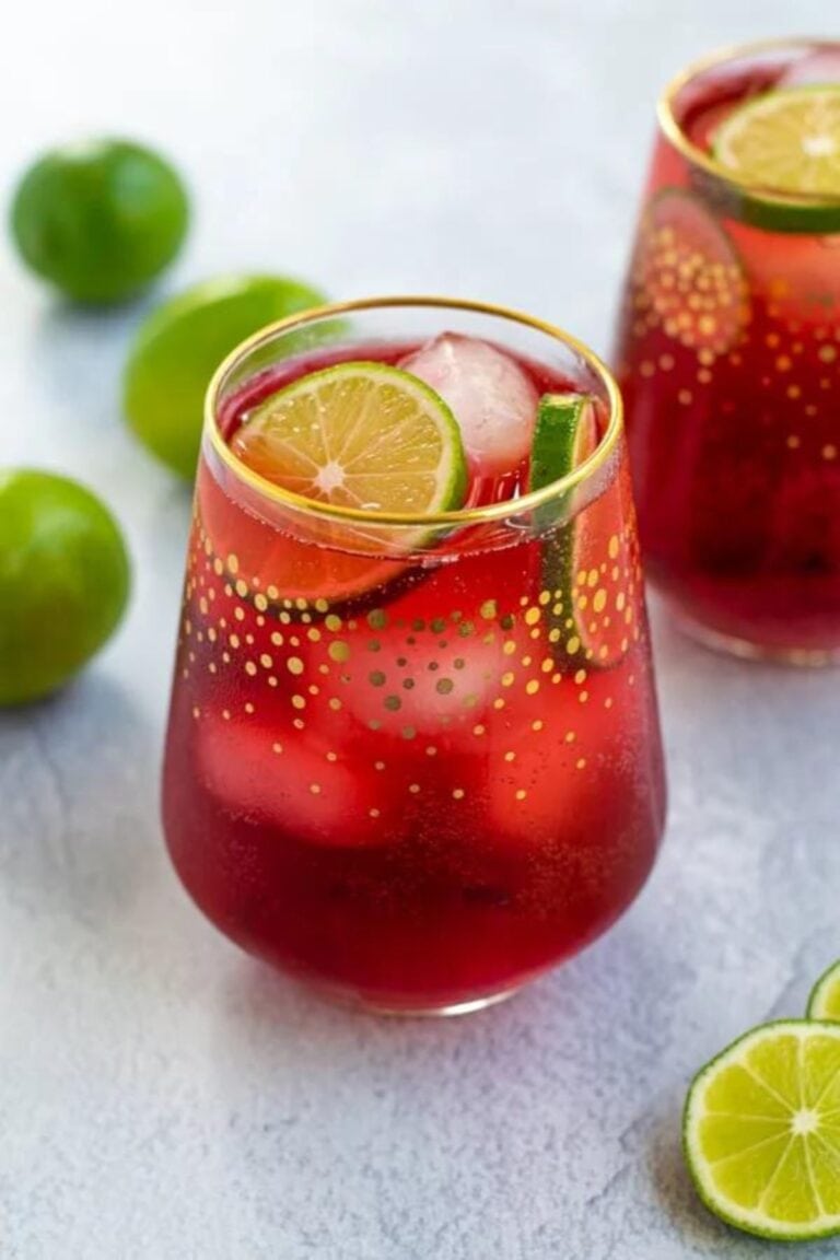 Glass of hibiscus iced tea sparkler garnished with lime slices.
