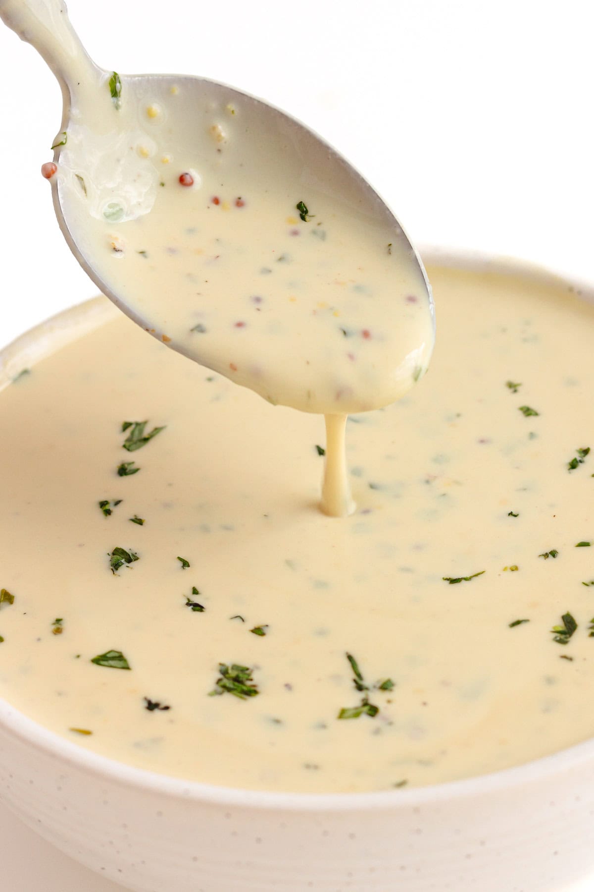 Spoon lifting mustard cream sauce from a small bowl.
