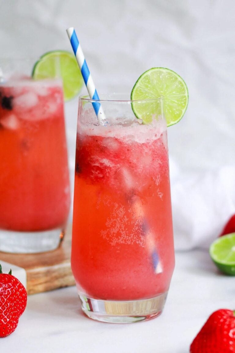 Glass of virgin strawberry margarita with a blue and white striped straw and lime slice.