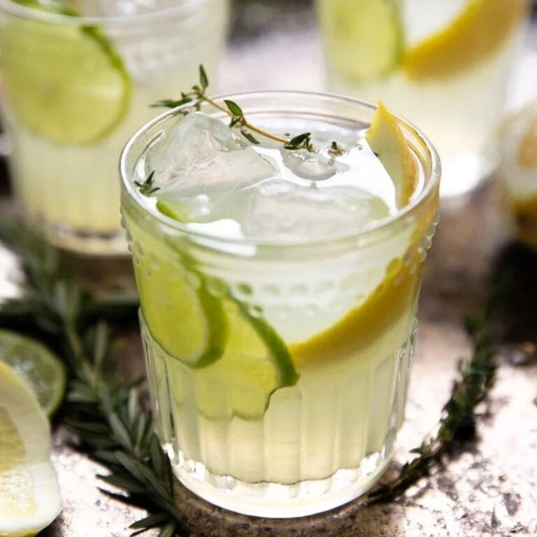 Glass of limoncello gin cocktail garnished with lemon, lime and fresh thyme.
