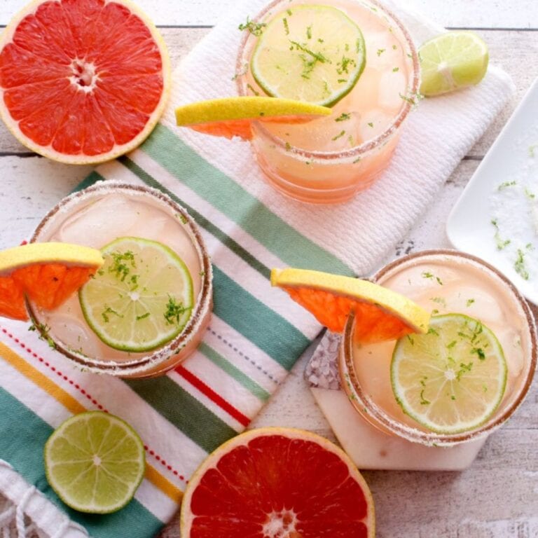 Overhead of three glasses of pink grapefruit margaritas garnished with grapefruit and lime.