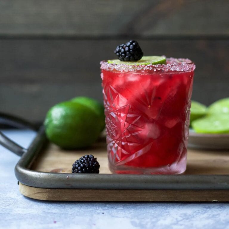 Glass of blackberry margarita on a wood tray with limes and blackberries.