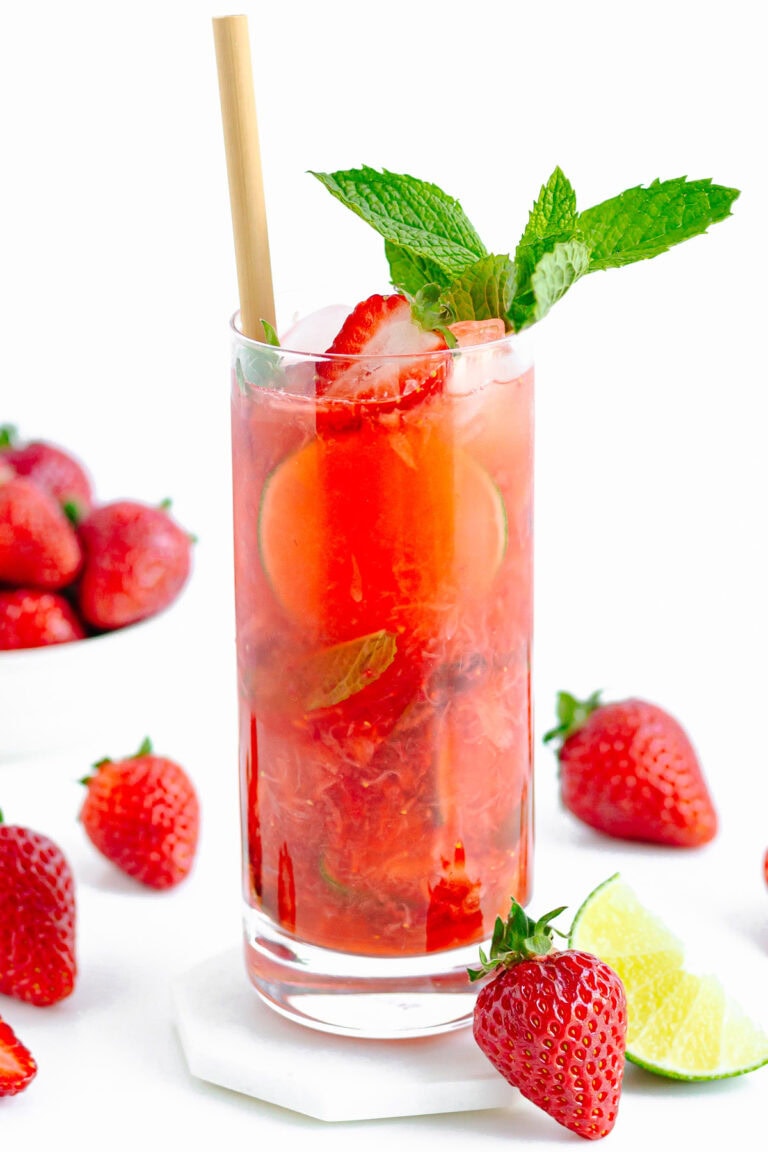 Tall glass of strawberry mojito mocktail surrounded by strawberries and lime.