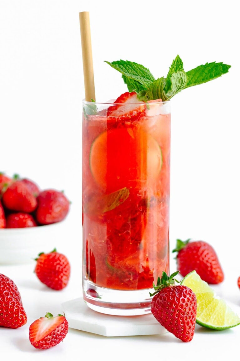 A tall glass of strawberry mojito mocktail garnished with mint, strawberries and lime.