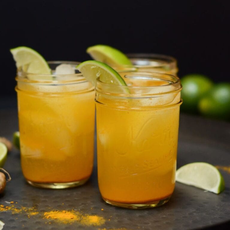 Turmeric gin and ginger cocktail in three mason jars garnished with lime wedges.