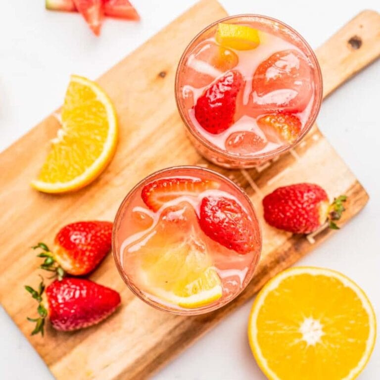 Overhead of two glasses of watermelon strawberry sangria on a wooden board with strawberries and orange slices.