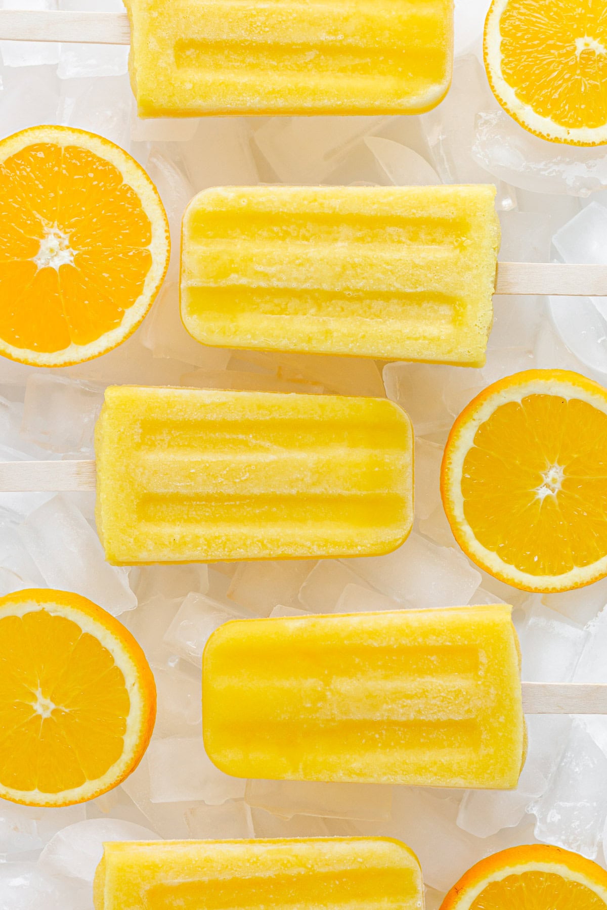 Overhead of homemade orange popsicles sitting on ice cubes with orange slices in between.