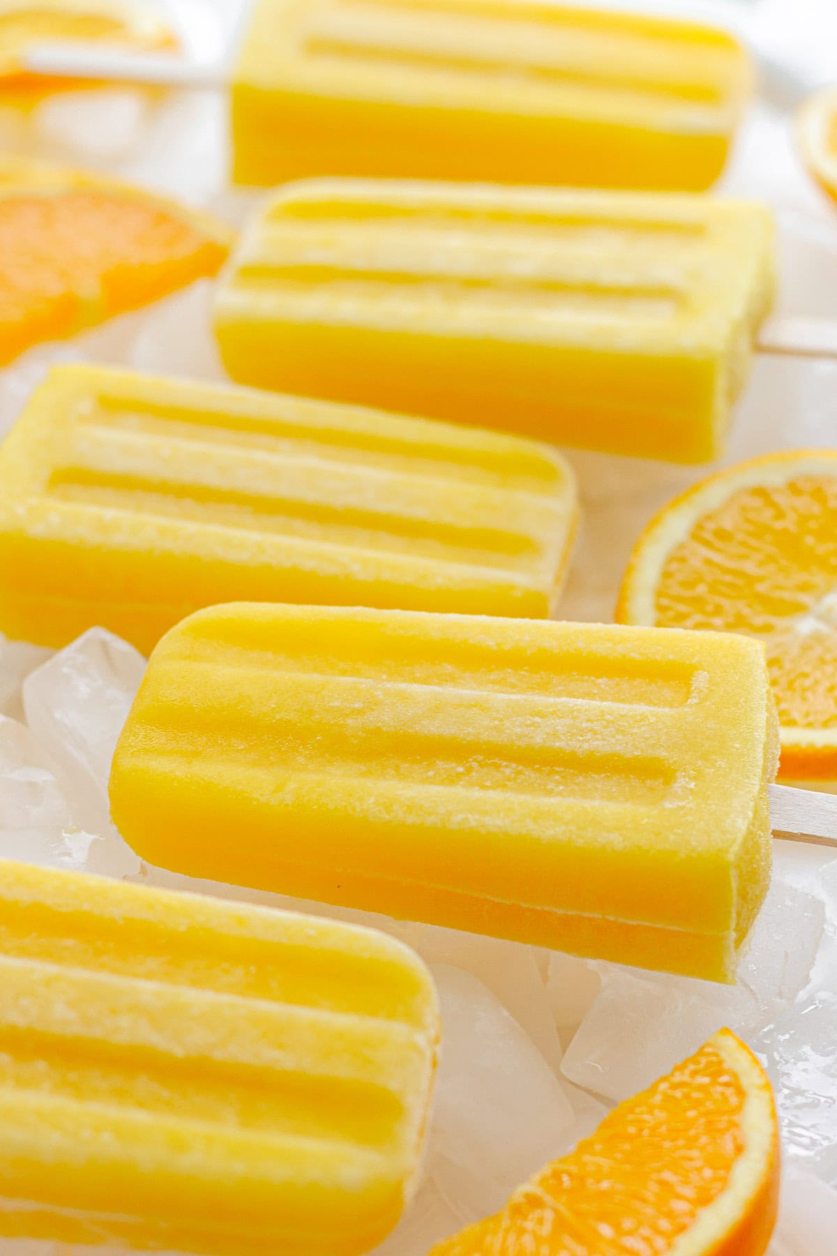 Orange popsicles lined up on ice cubes with some orange slices.