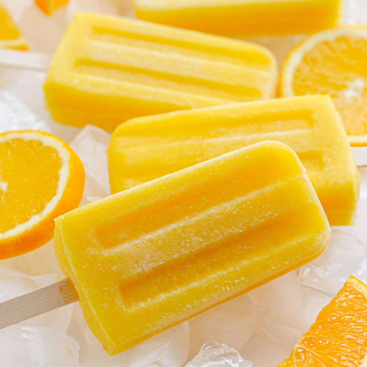 Orange popsicles sitting on ice with orange slices.