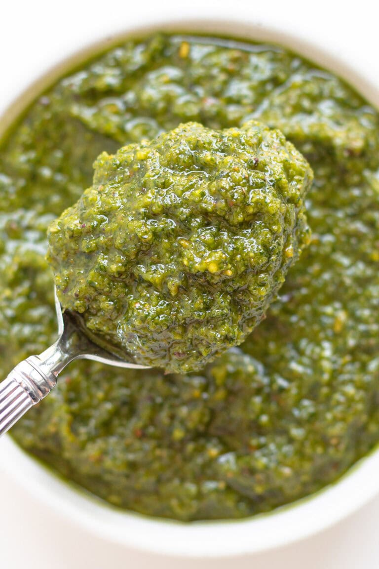 Spoonful of pistachio pesto lifted above a small white bowl of pesto.