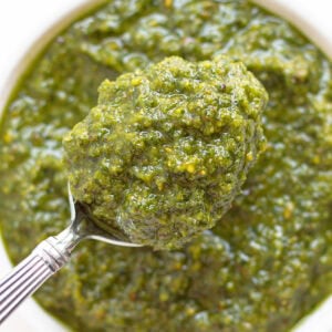 Spoon of pistachio pesto lifting up from bowl.