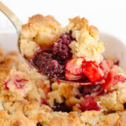 Serving spoon scooping up some apple and blackberry crumble from the baking dish.