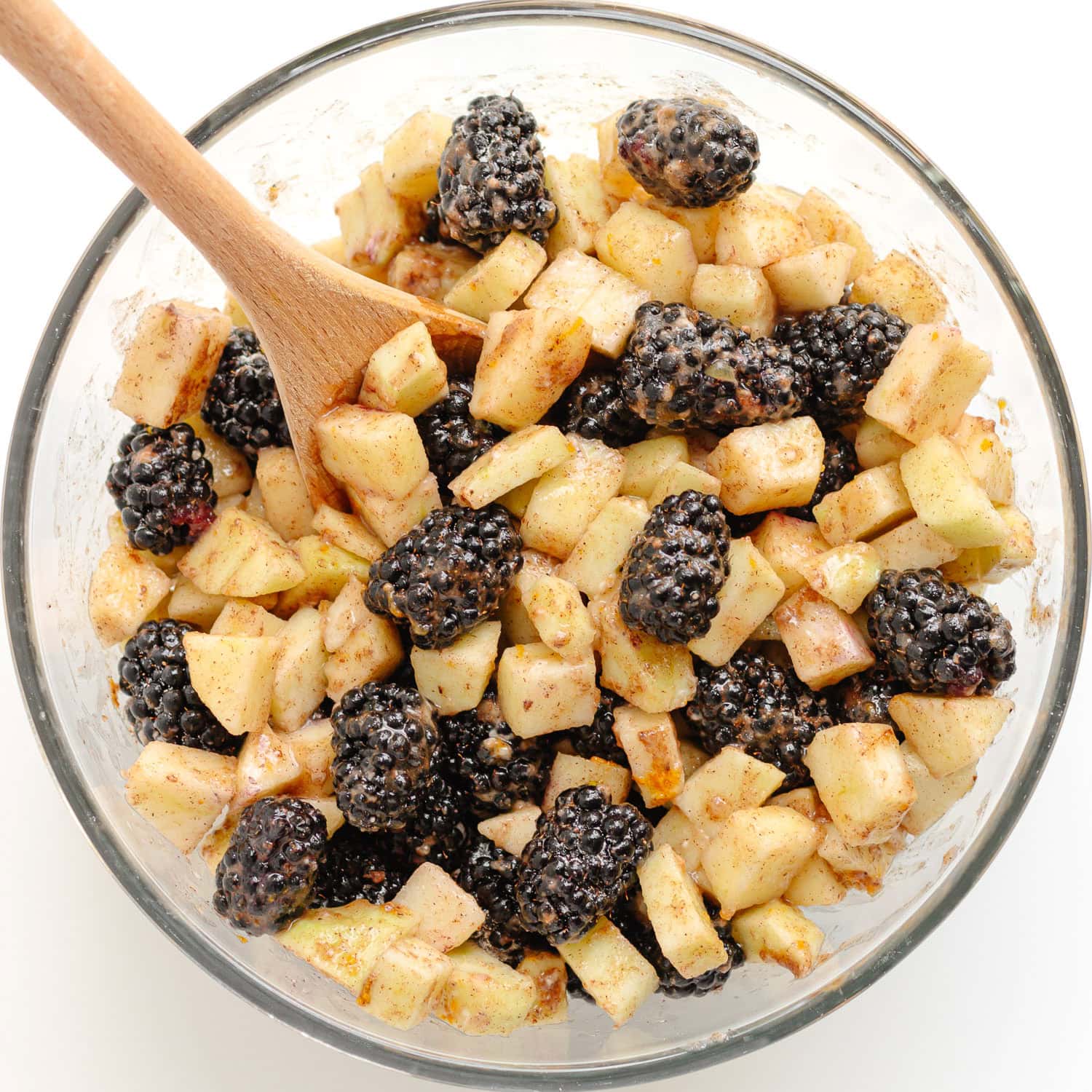 The fruit mixture for an apple blackberry crumble in a glass mixing bowl.