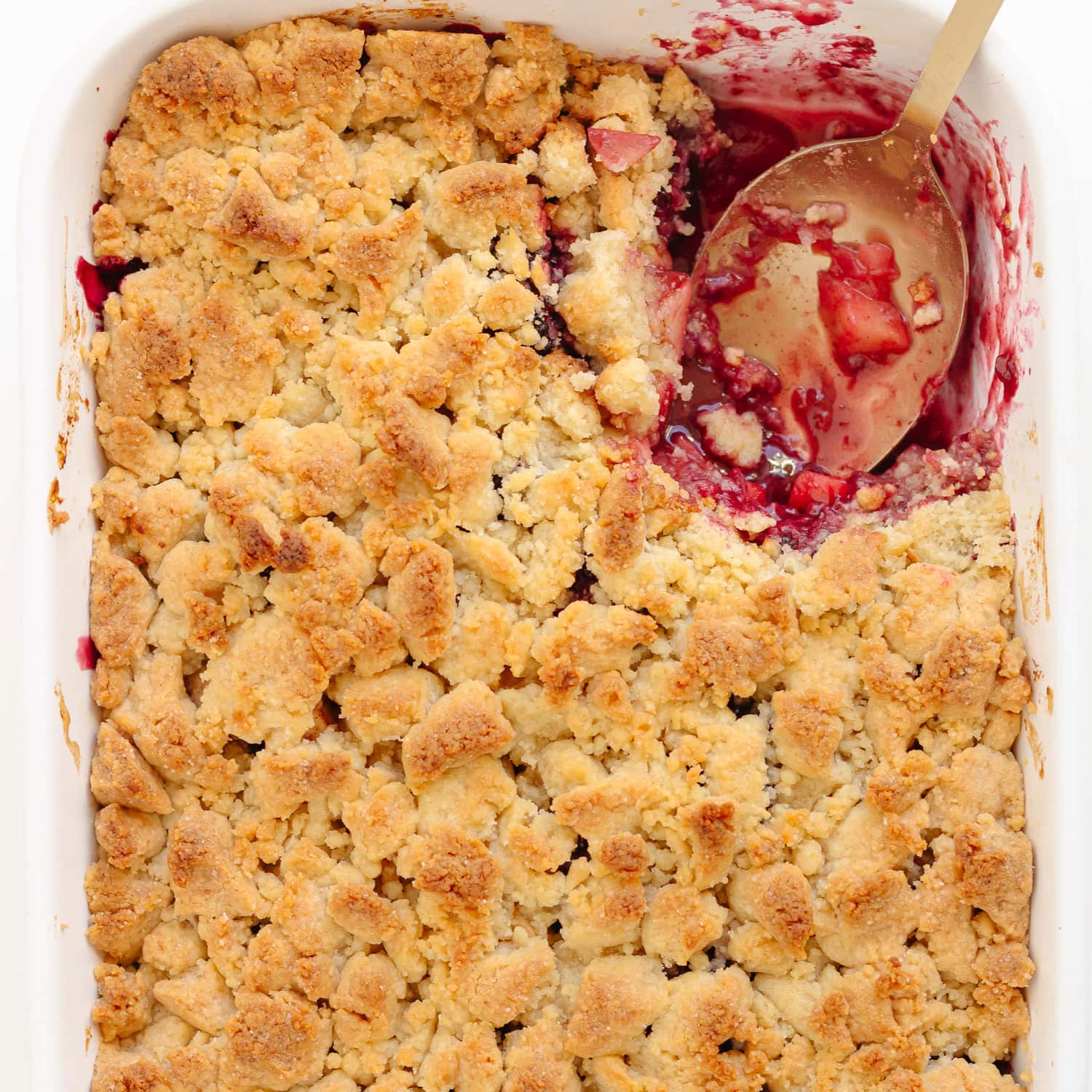 Apple blackberry crumble in a white baking dish with a scoop taken out.