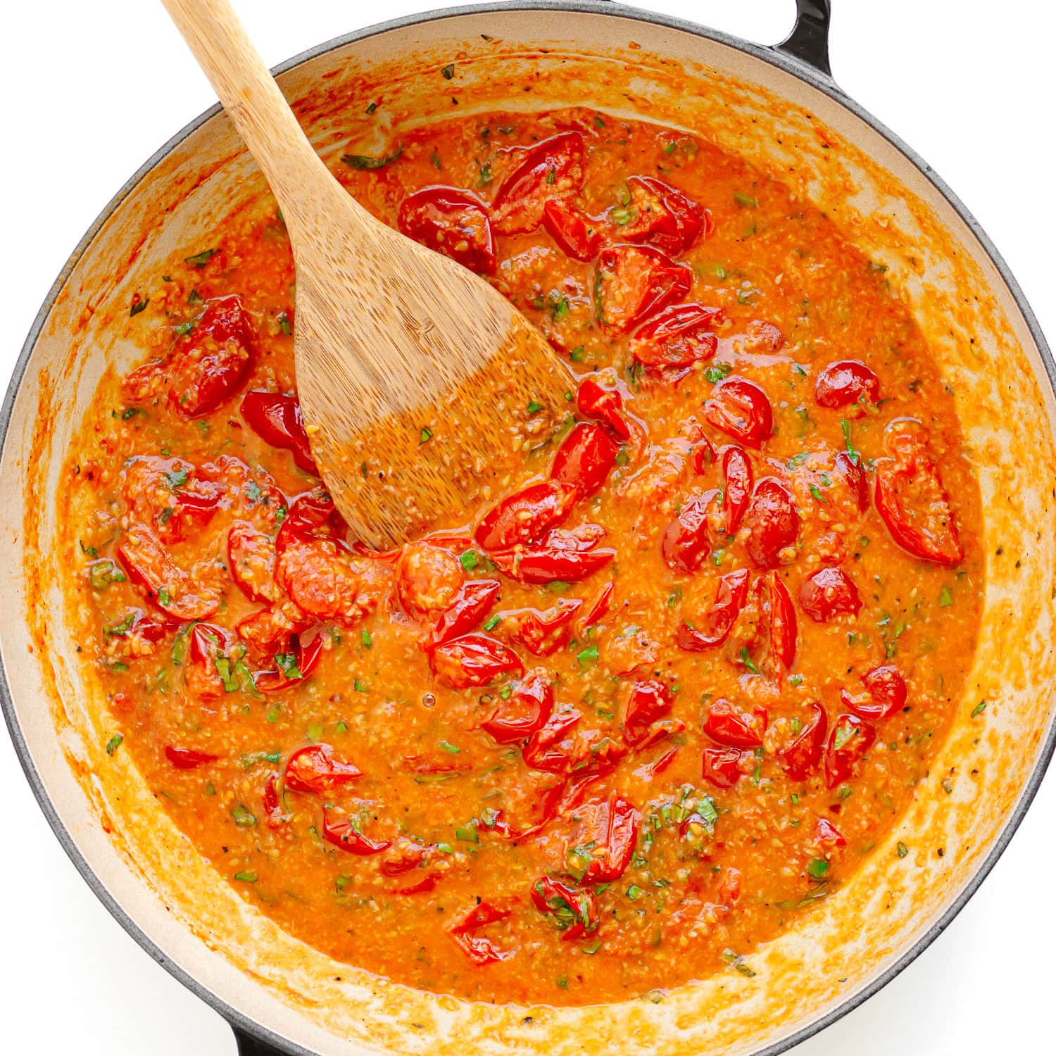 Cherry tomato garlic butter sauce in a large pan with a wooden spoon.