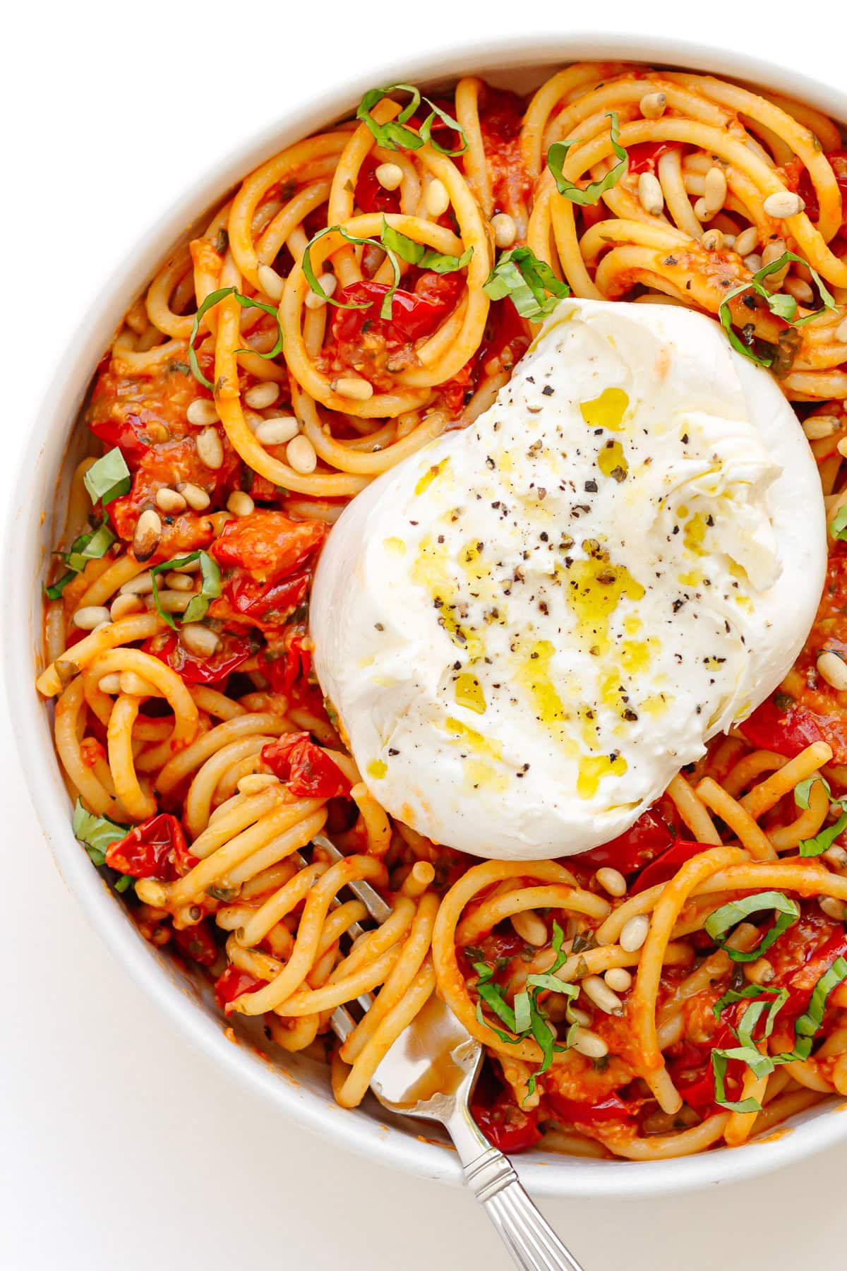 Cherry tomato pasta topped with a ball of burrata and garnished with pine nuts and fresh basil.