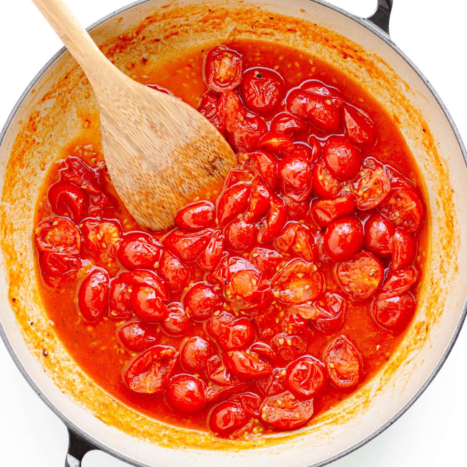 Cherry tomatoes being cooked down for sauce in a large pan.