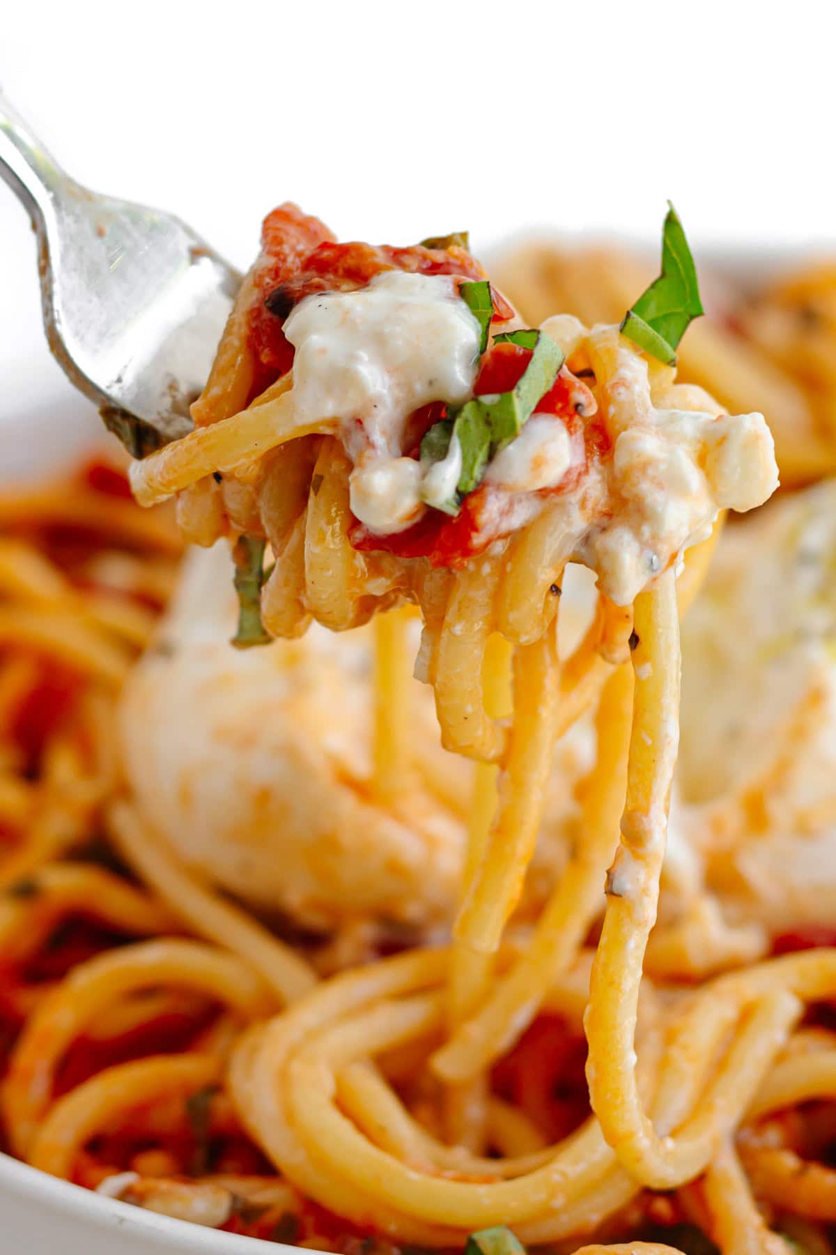 Fork lifting up some tomato burrata pasta from plate.