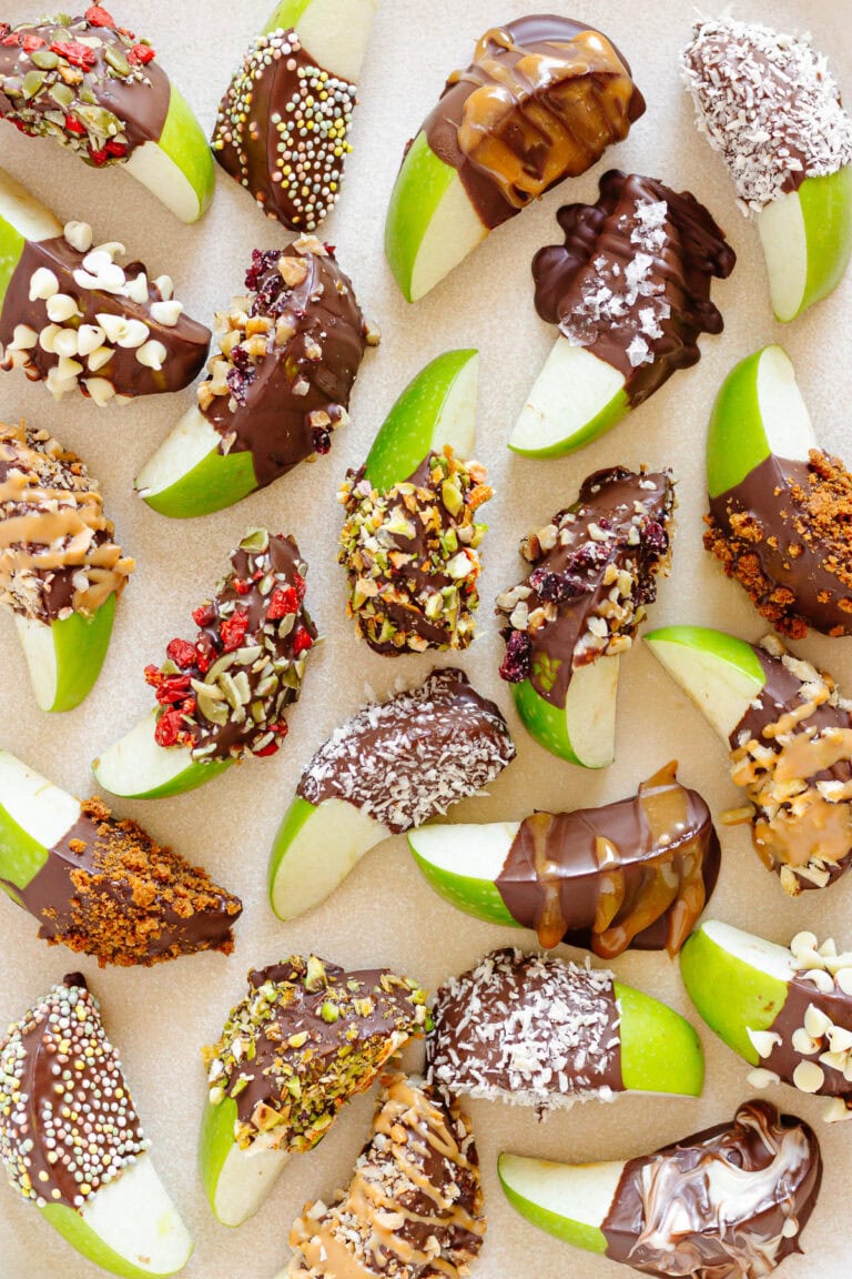 Chocolate apple slices dipped in a variety of toppings on a cream colored platter.