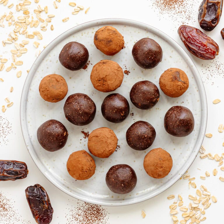 Plate of chocolate bliss balls surrounded by Medjool dates, rolled oats and cocoa powder.