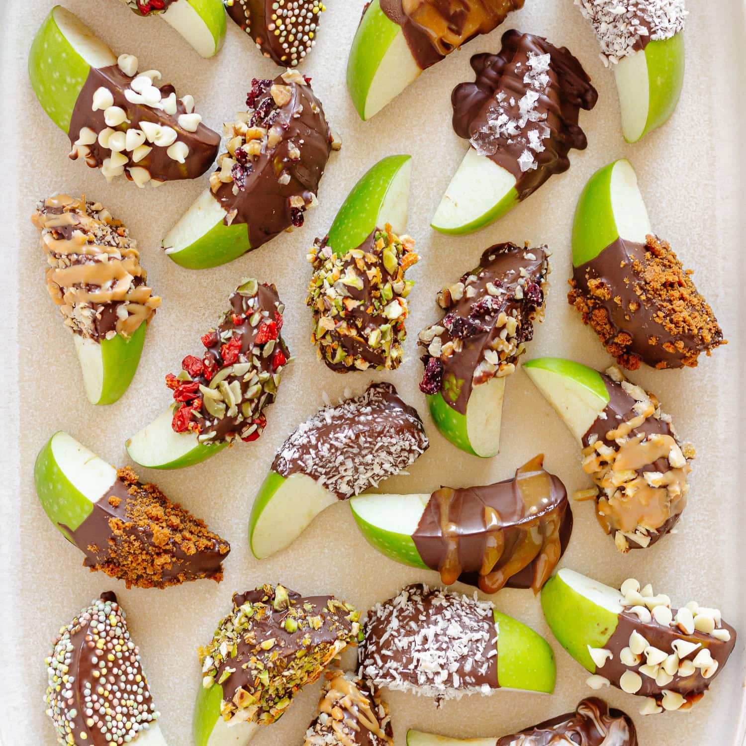 A variety of chocolate dipped apple slices on a cream colored serving platter.