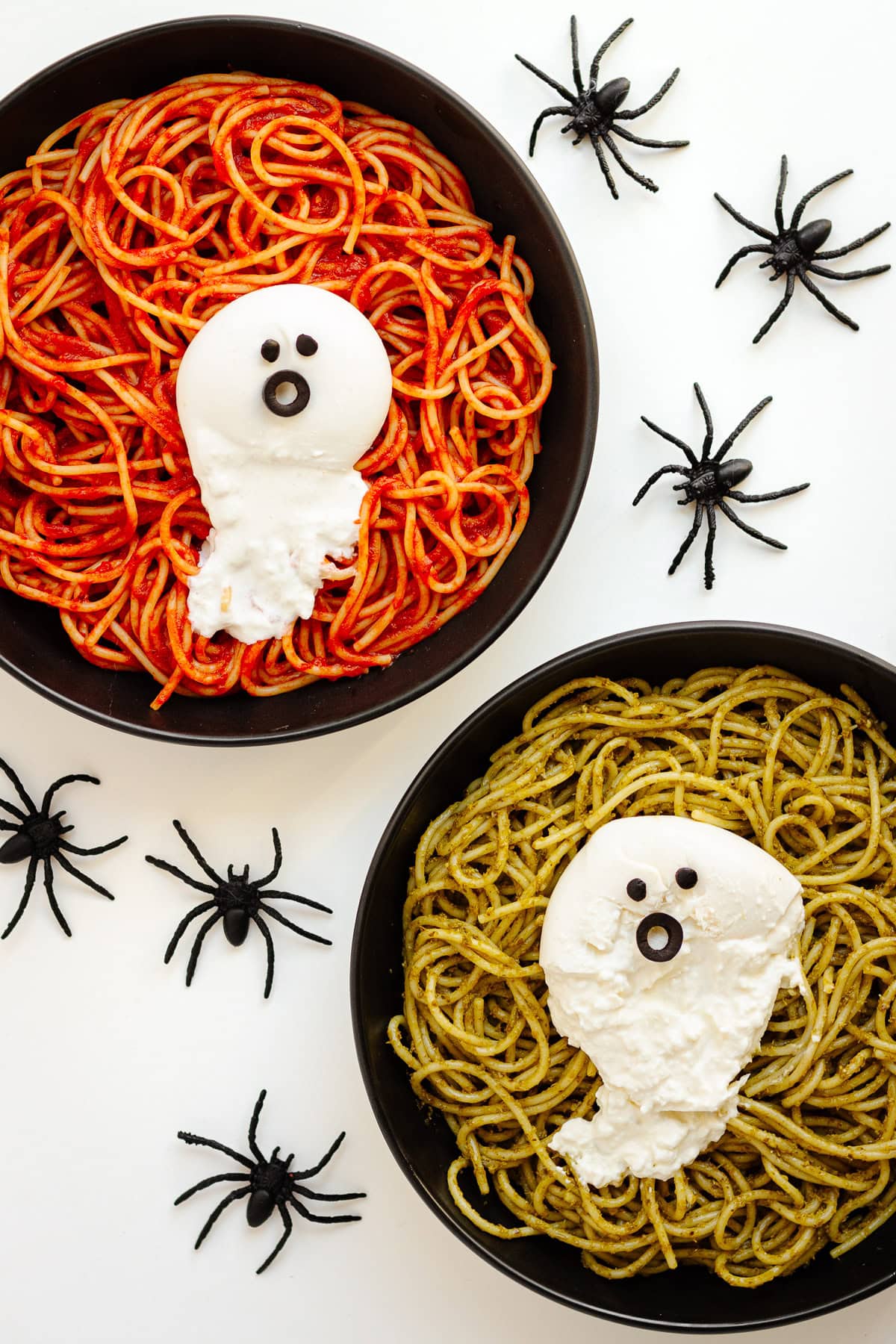 Two black plates of pasta topped with burrata ghosts and surrounded by spiders.