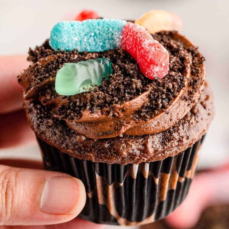 Hand holding a Halloween dirt cupcake topped with gummy worms.