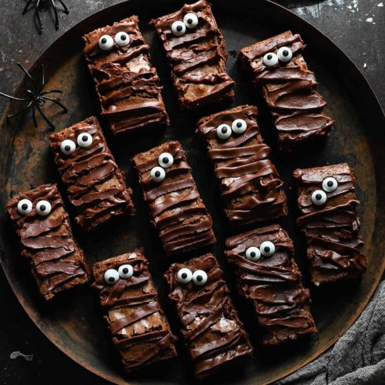 Halloween mummy brownies with chocolate ganache frosting on a black plate.