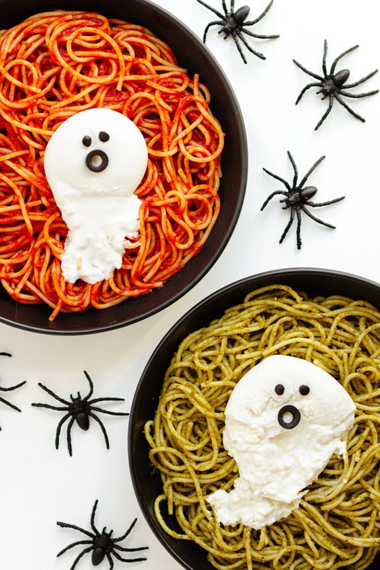Two plates of spaghetti (one with tomato sauce and the other with pesto) with ghosts made from burrata on top.