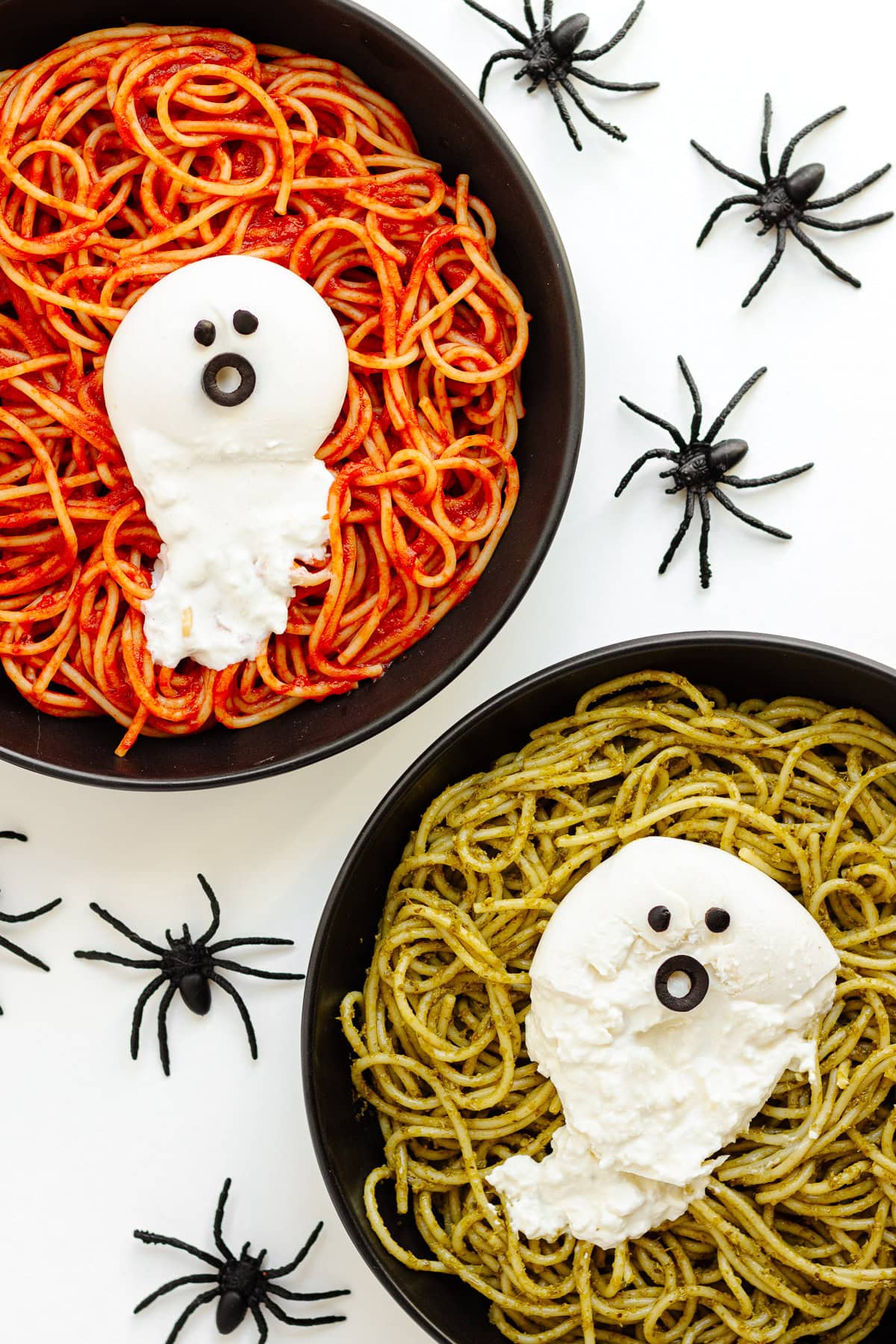 Two plates of spaghetti (one with tomato sauce and the other with pesto) with ghosts made from burrata on top.