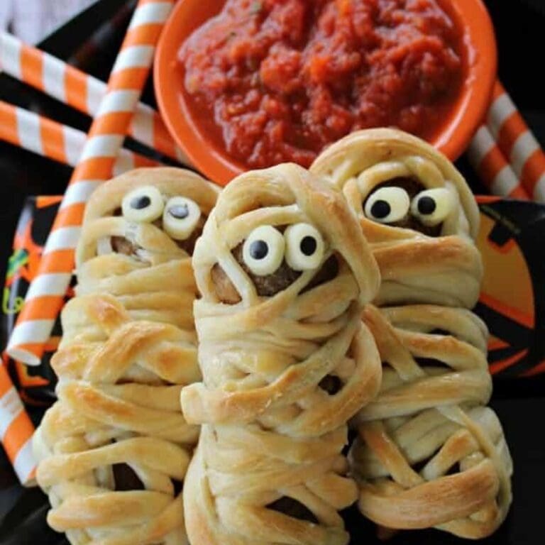 Three meatball mummies next to a bowl of marinara sauce.